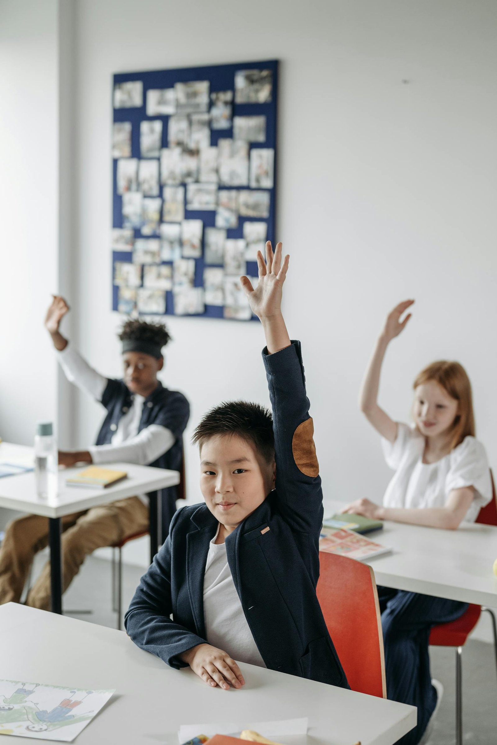 Children in a modern classroom raise hands during an engaging lesson.